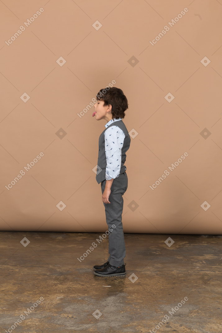 Вид сбоку симпатичного мальчика в костюме, показывающего язык