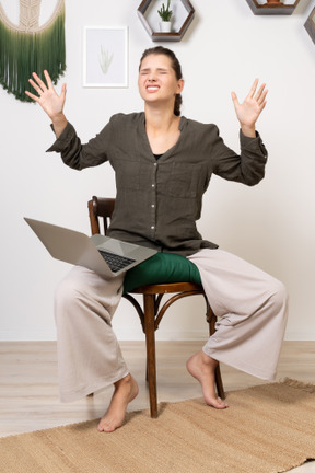 Vorderansicht einer gereizten jungen frau mit kopfschmerzen, die mit einem laptop auf einem stuhl sitzt