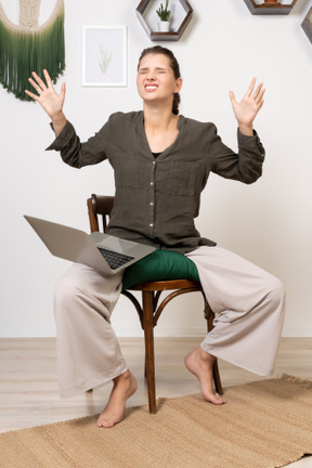 Vue de face d'une jeune femme irritée avec un mal de tête assise sur une chaise avec un ordinateur portable