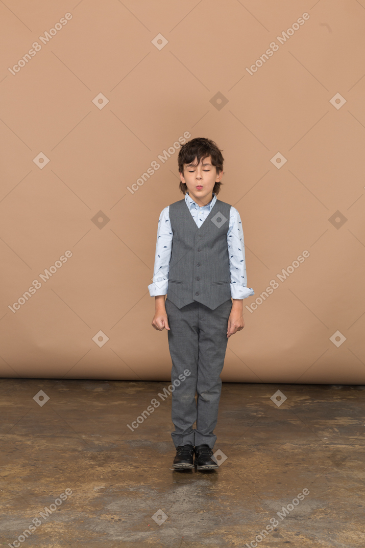 Front view of a cute boy in grey suit standing with closed eyes