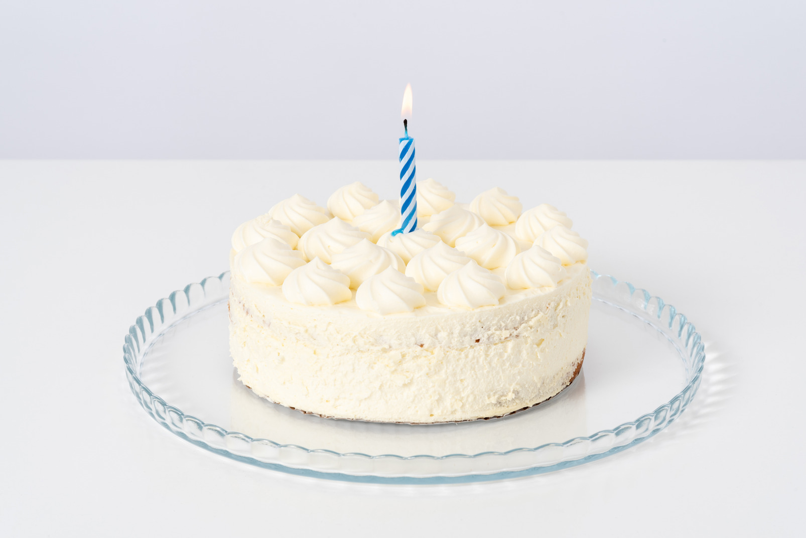 White cake with a candle on a glass plate