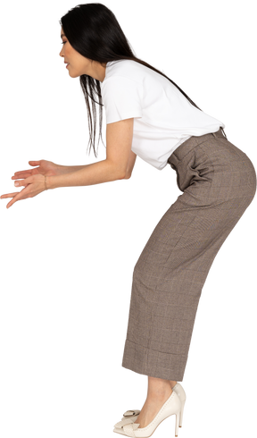 Vista lateral de uma jovem questionadora de calça e camiseta, levantando as mãos e se curvando