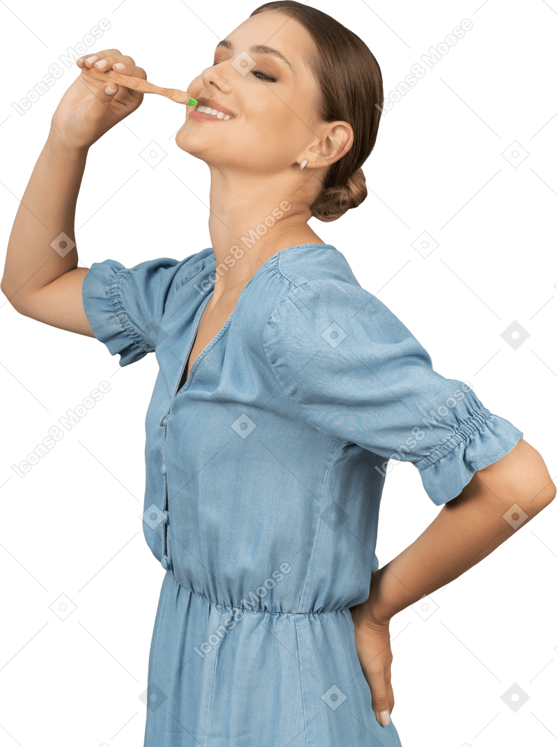Vista di tre quarti di una giovane donna in abito blu che si lava i denti