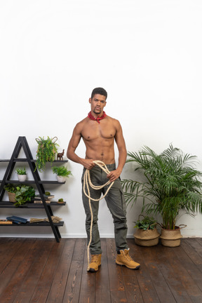 Front view of young man standing and holding a coil of rope and looking at camera