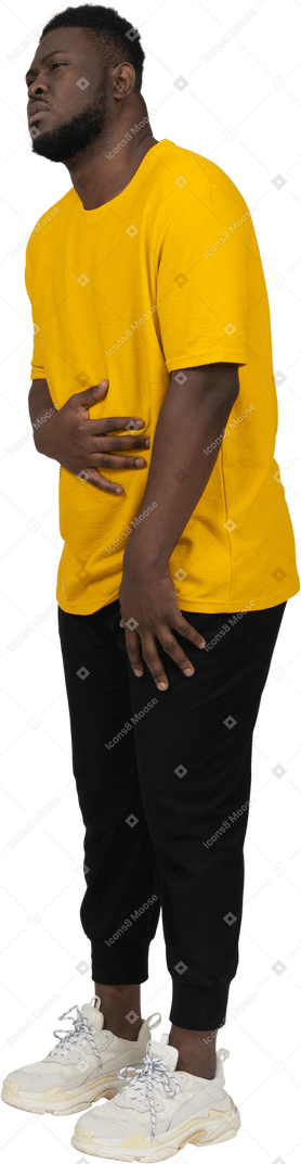 Three-quarter view of a young dark-skinned man in yellow t-shirt touching stomach