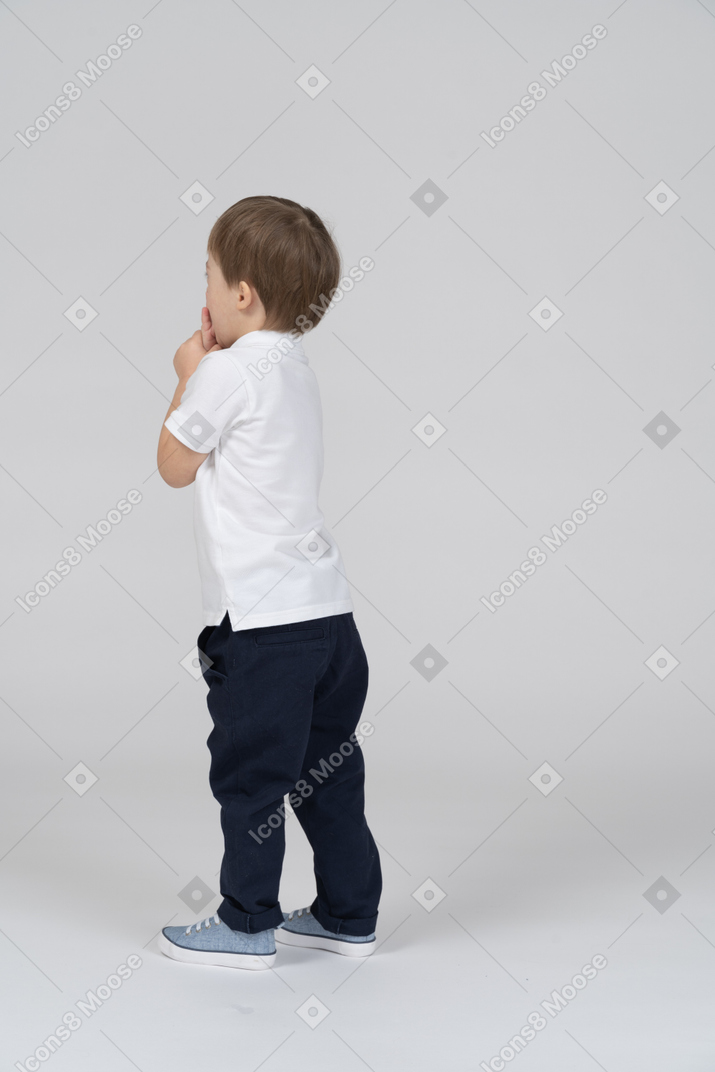 A boy standing in front of a wall with his hands folded
