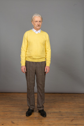 一个不高兴的老人穿着黄色套头衫，看着相机的前视图
