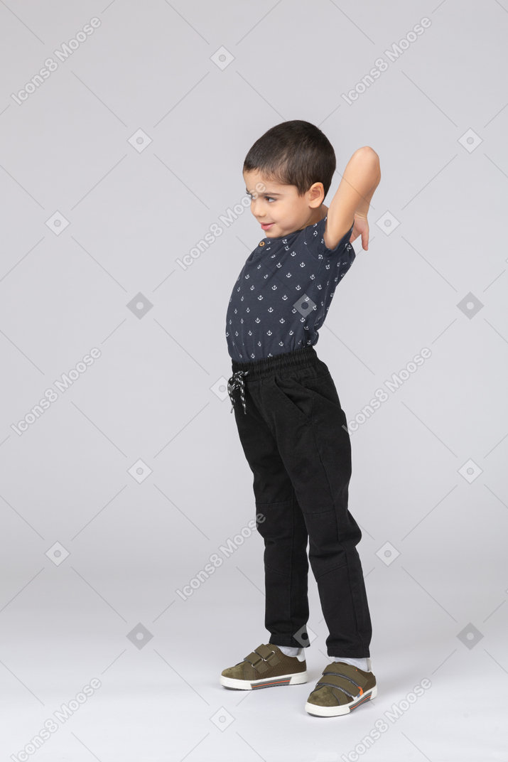 Side view of a cute boy in casual clothes stretching with hands behind head