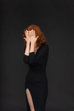A frontal view of the sexy young girl dressed in black and covering her face with hands