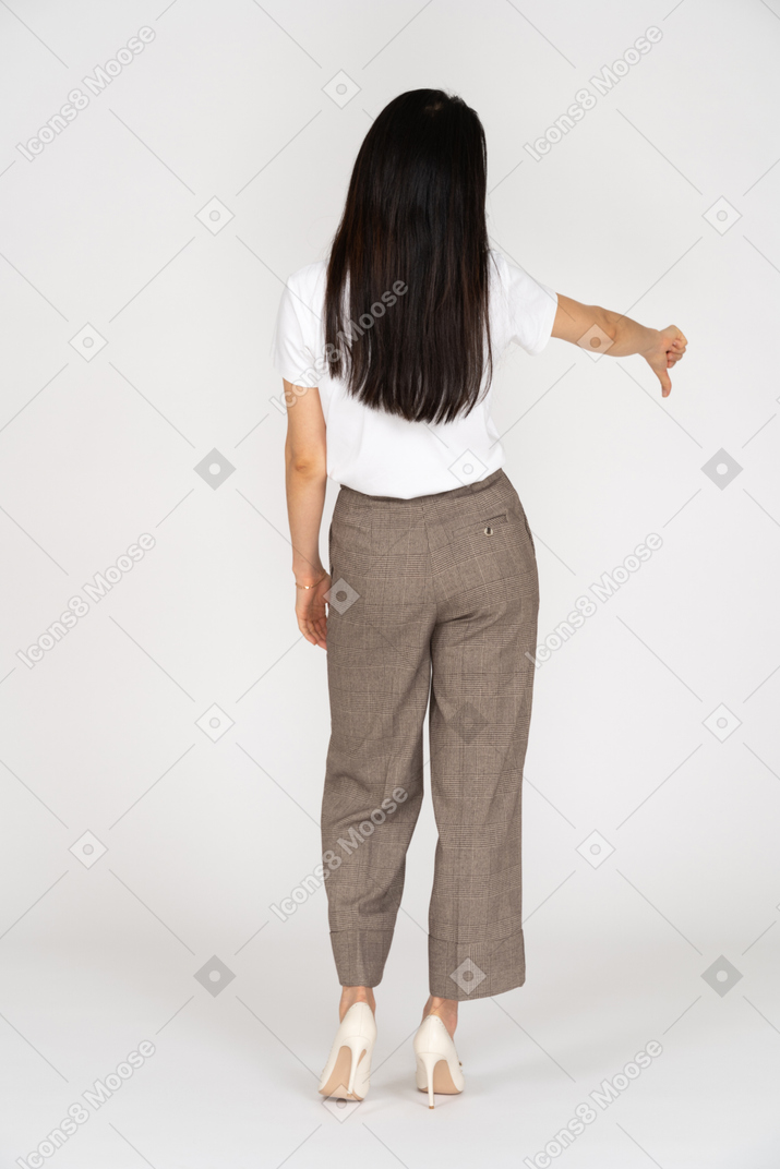Vista posteriore di una giovane donna in calzoni e maglietta che mostra il pollice verso il basso