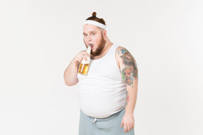 A fat man in sportswear drinking beer from the bottle