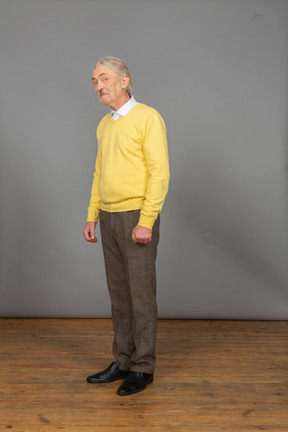 Three-quarter view of an old man in a yellow pullover showing tongue and looking at camera