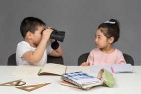 男孩通过双筒望远镜看着他的妹妹