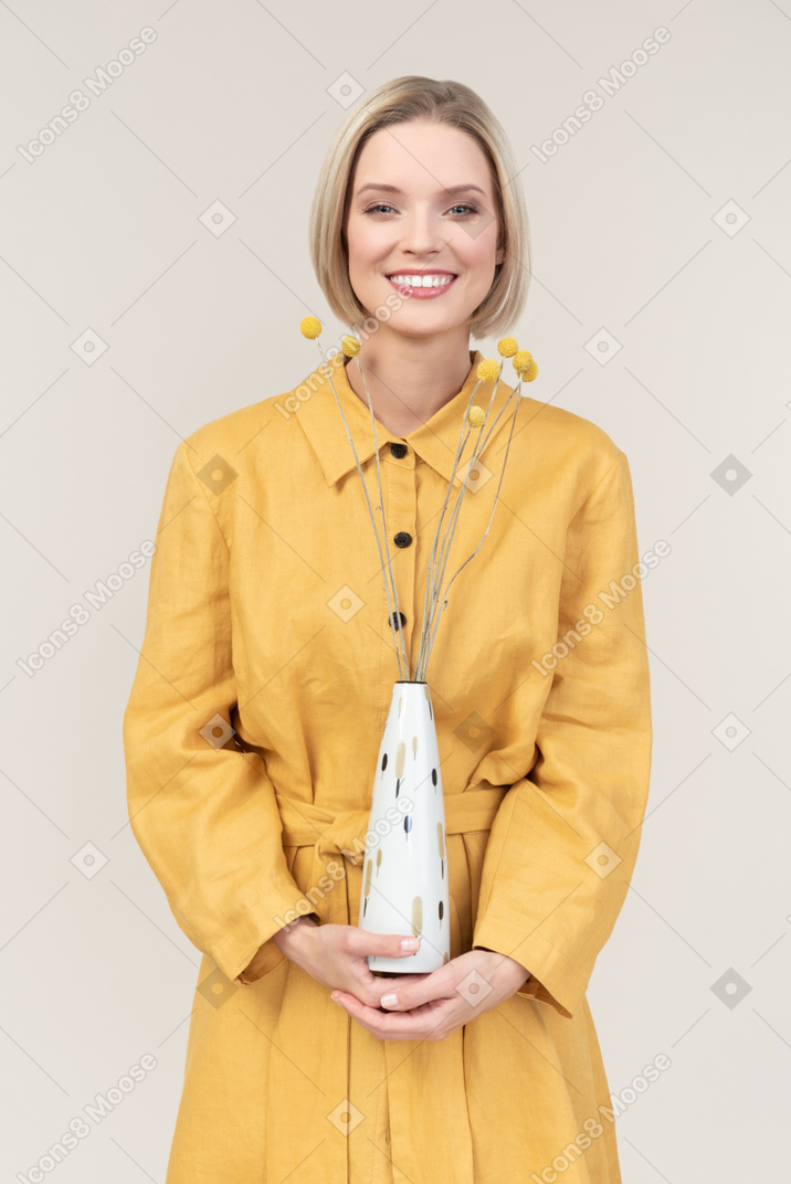 Souriante jeune femme tenant un vase avec des brindilles séchées