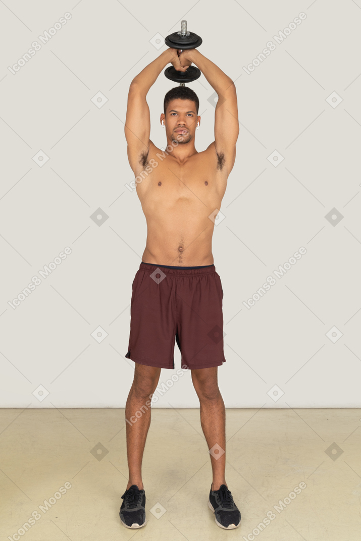 Front view of young athletic man doing exercises with dumbbell