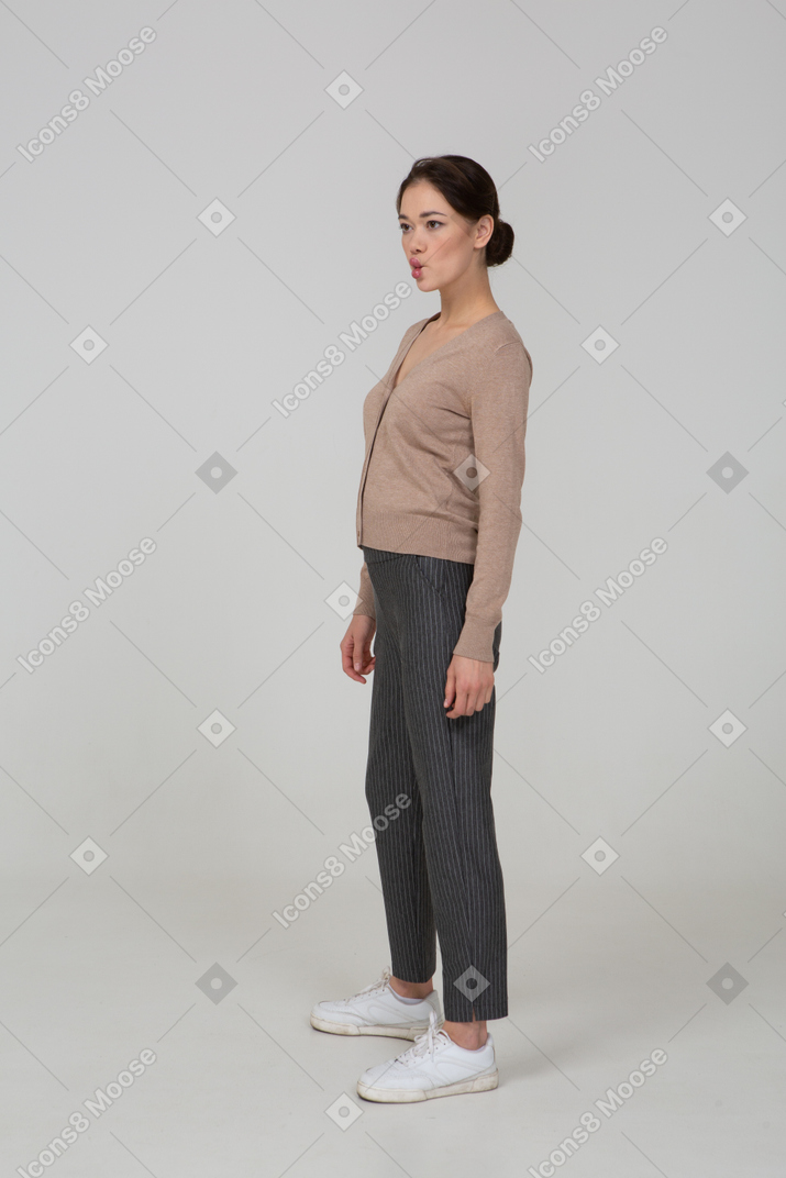 Vista de tres cuartos de una dama haciendo pucheros en suéter y pantalones mirando a un lado