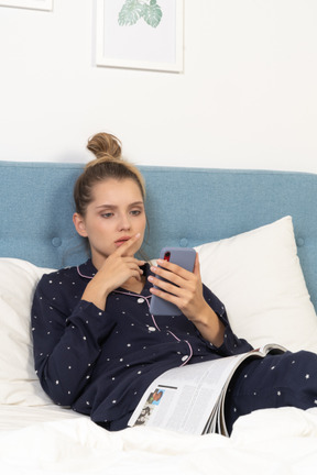 Young woman lying in bed in pajamas and looking at her phone