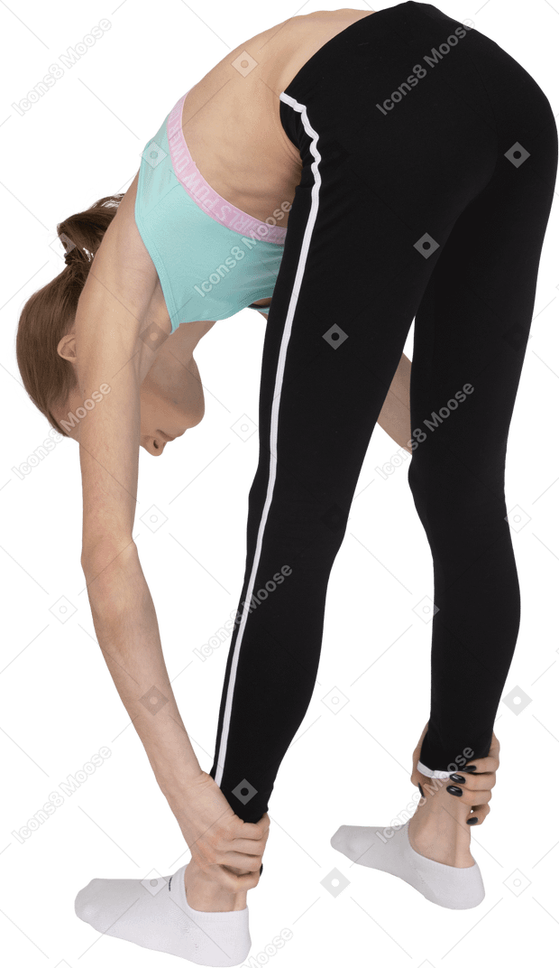 Vista traseira de três quartos de uma adolescente em roupas esportivas, alongando-se e segurando os tornozelos