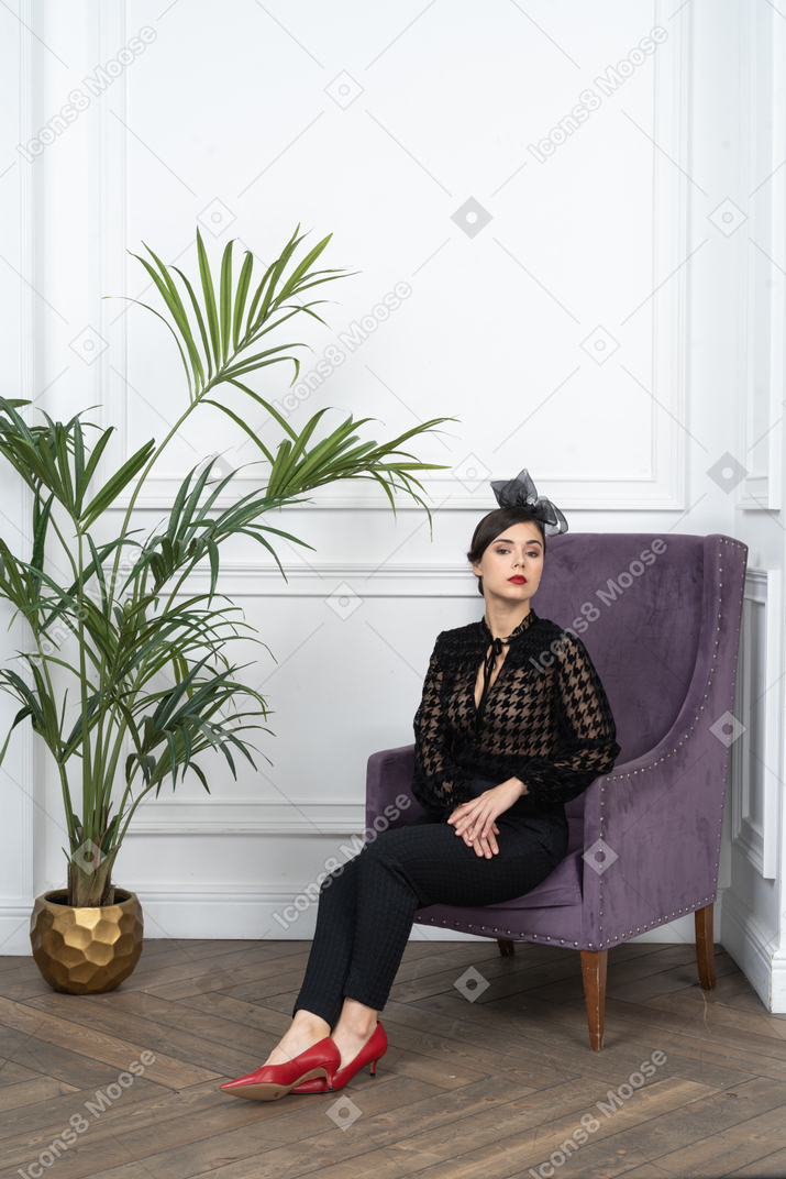 A woman sitting on a purple chair next to a potted plant