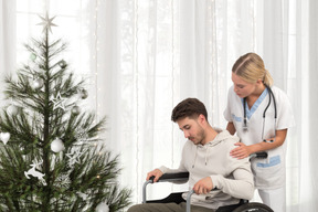 Enfermera ayudando al hombre en silla de ruedas a obtener su regalo de navidad