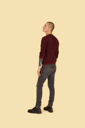 Three-quarter back view of a funny grimacing young man in read sweater