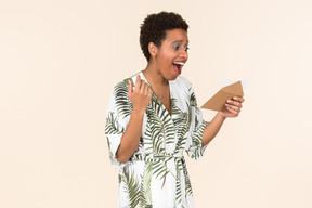 Black short-haired woman in a white and green dress, standing with an envelope in her hand