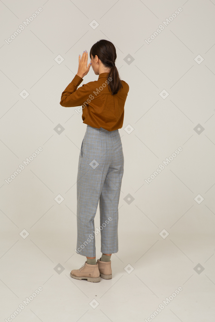 Three-quarter back view of a young asian female in breeches and blouse raising hands