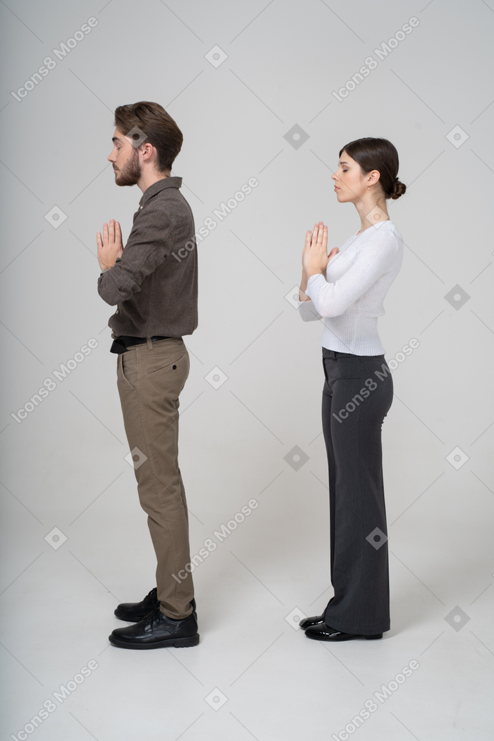 一緒に手を繋いでいる事務服で祈る若いカップルの側面図