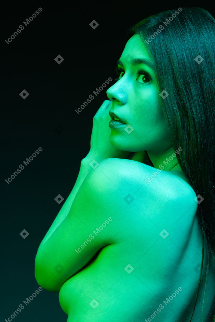 Side shot of a young woman shirtless under green light
