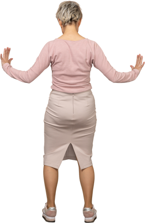 伸ばした腕で立っているカジュアルな服装の女性の背面図