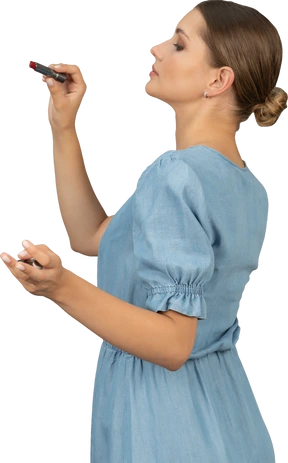 Side view of a young woman in blue dress holding a lipstick