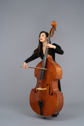 Three-quarter view of a young woman in black dress playing the double-bass with a bow