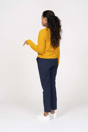 Vista traseira de uma garota com roupas casuais apontando para baixo com um dedo