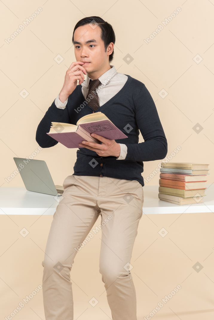 Young asian student biting his finger while reading a book