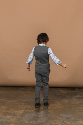 Вид сзади на мальчика в костюме, стоящего с распростертыми руками