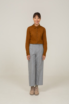 Vista frontale di una giovane donna asiatica sorridente in calzoni e camicetta in piedi ancora