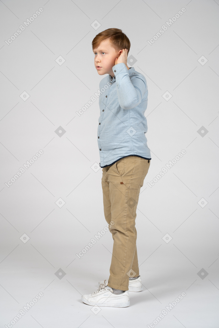 Vista lateral de um menino mantendo a mão perto da orelha e ouvindo atentamente