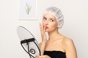 Mujer con gorra médica sosteniendo un espejo y tocándose los labios