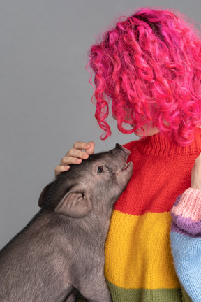 A pink haired female stroking a small pet pig