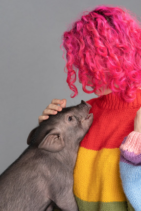 Une femme aux cheveux roses caressant un petit cochon