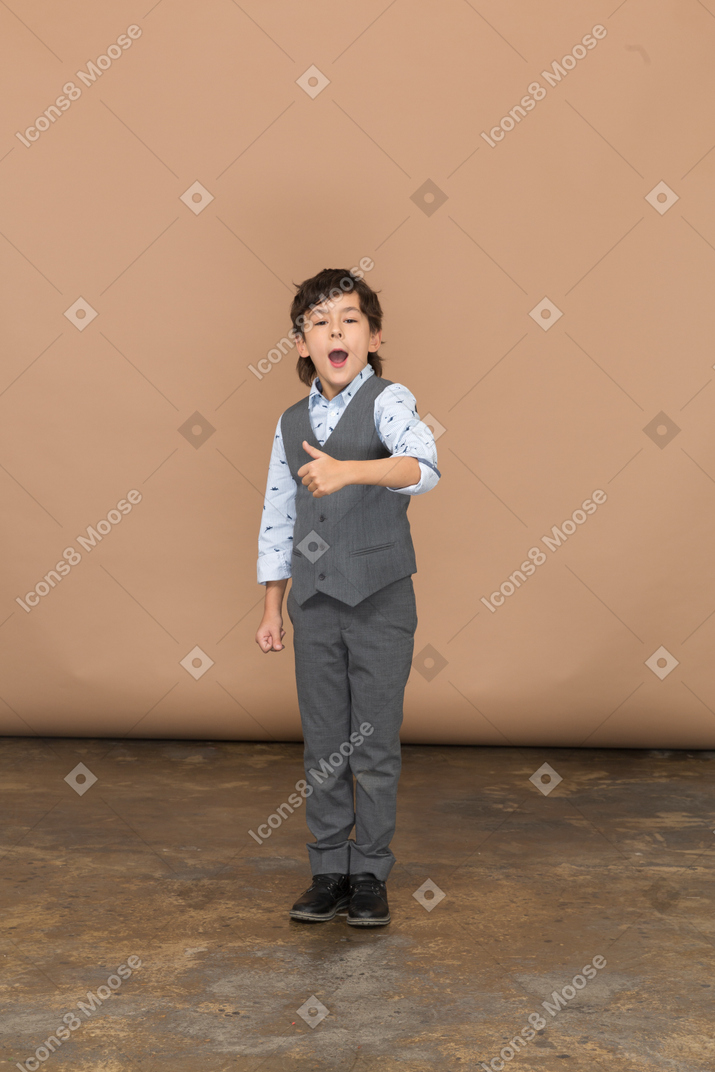 Vista frontale di un ragazzo carino in abito grigio che mostra il pollice in su