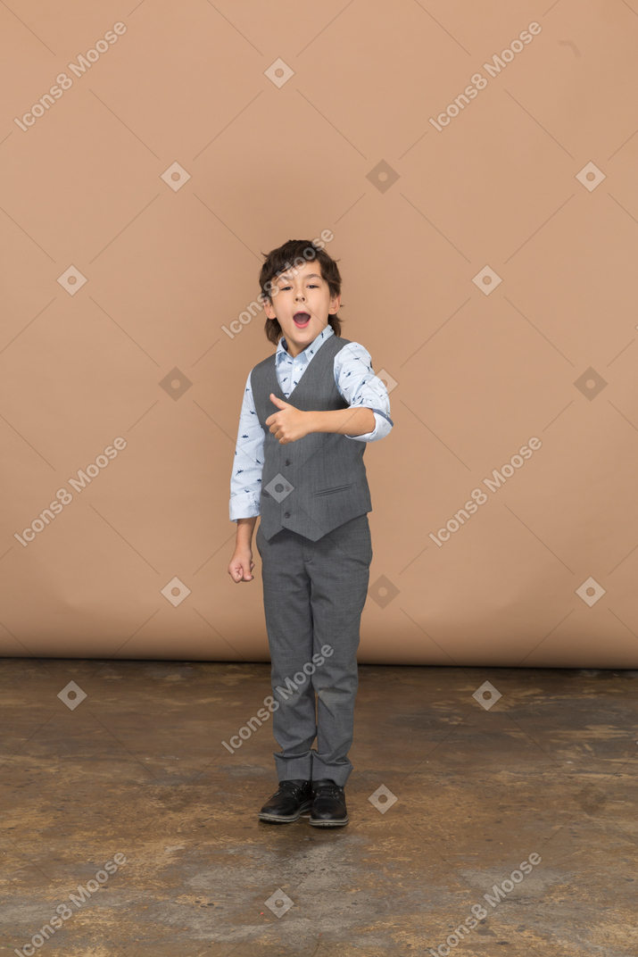 Front view of a cute boy in grey suit showing thumb up