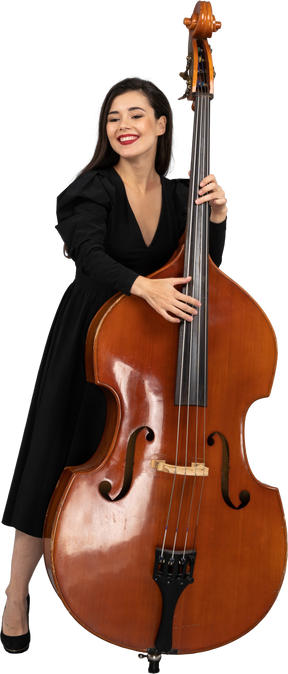 Vista frontale di una giovane donna sorridente in abito nero che suona il contrabbasso