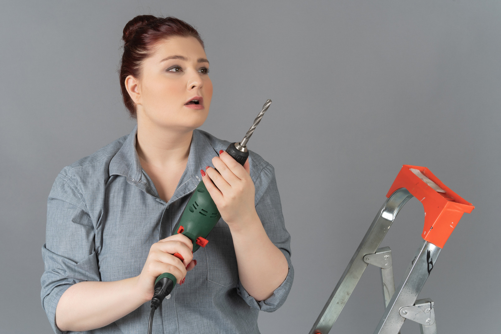 Young woman looking surprisingly sideways and holding a drill