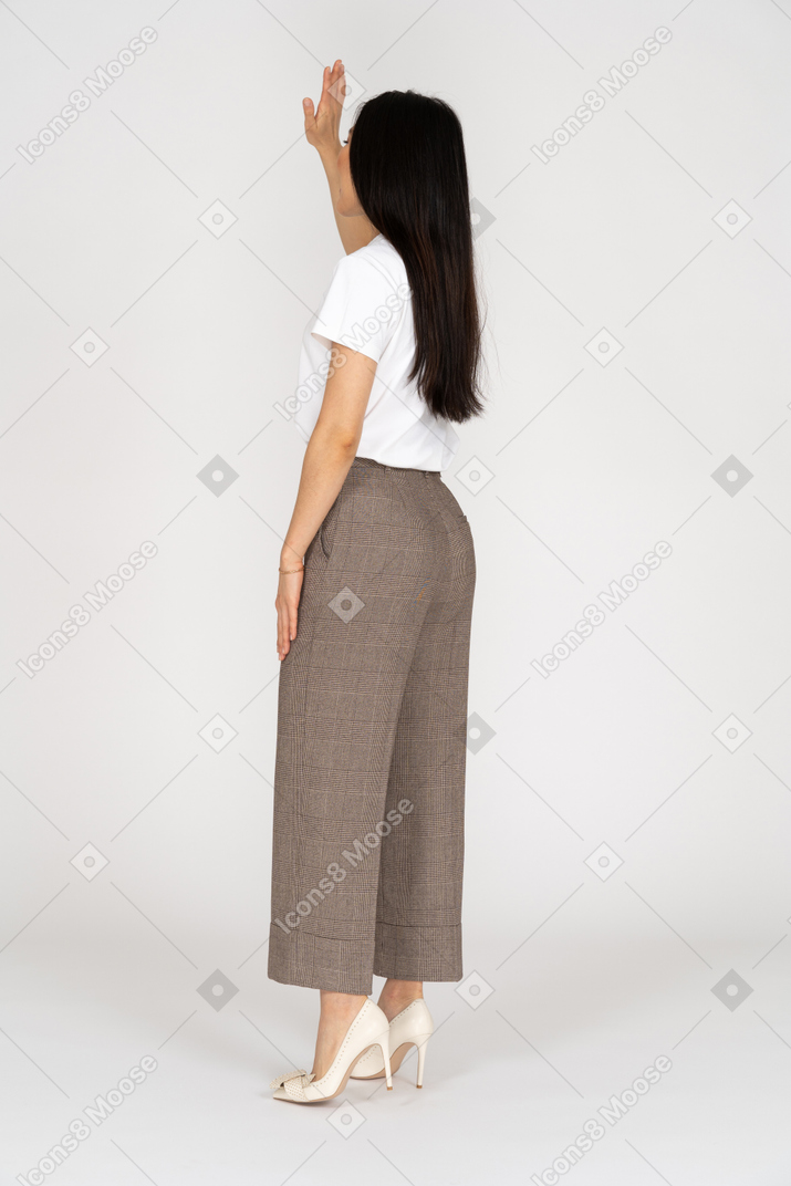 Vista posterior de tres cuartos de una mujer joven en calzones levantando su mano