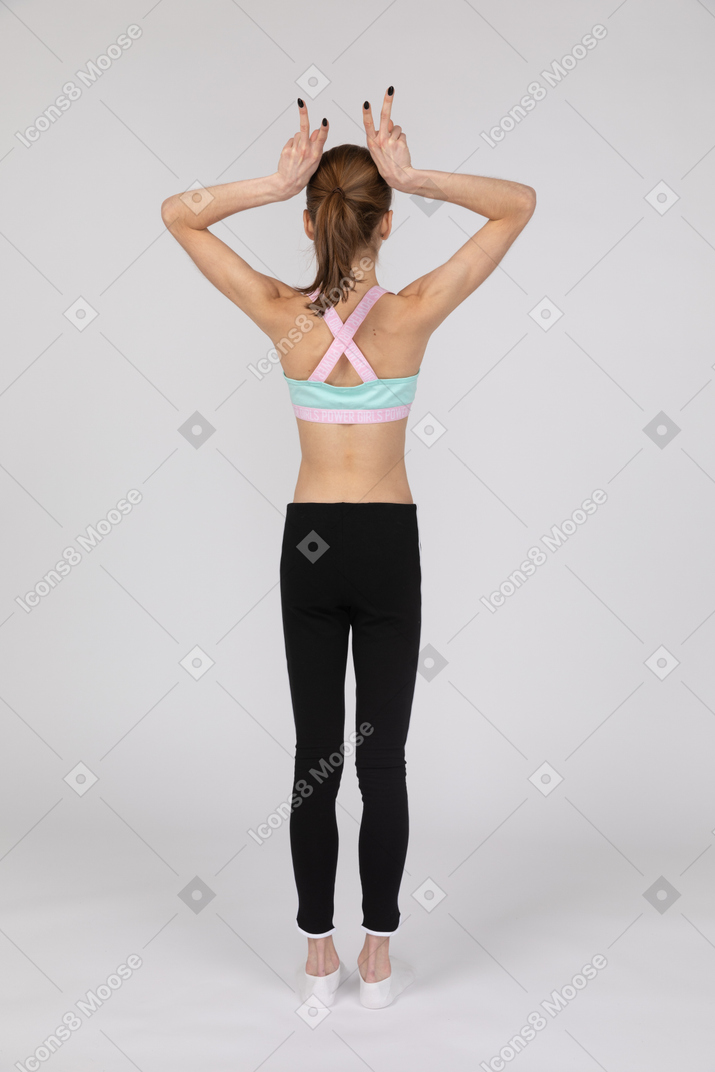 Vista posterior de una jovencita en ropa deportiva haciendo cuernos