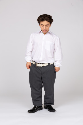 Молодой человек в рубашке и брюках смотрит вниз