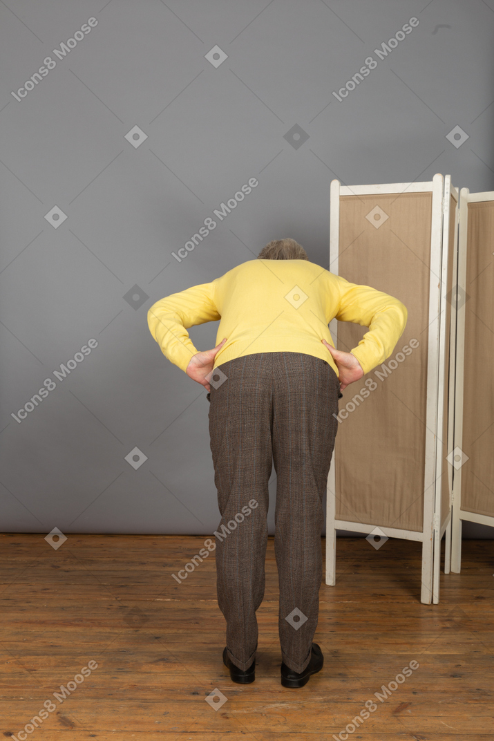 Back view of an old man putting hands on hips while leaning forward