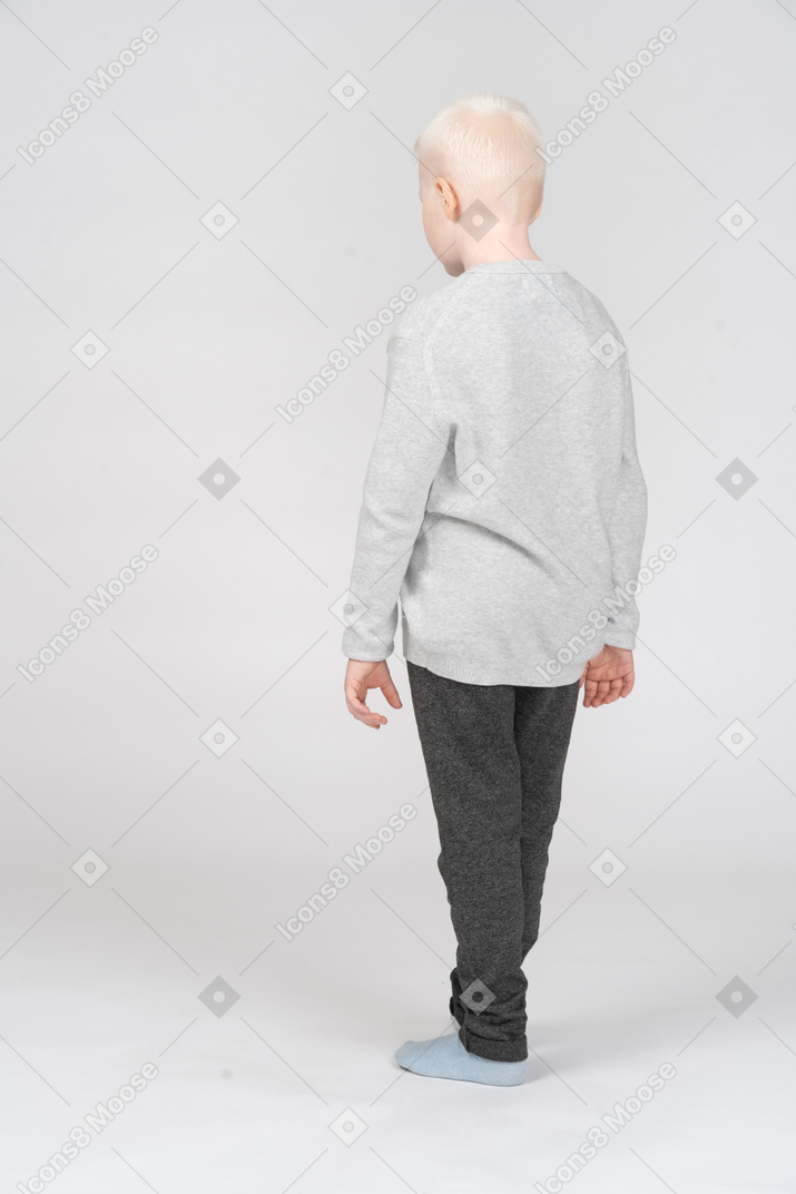 Back view of a little blond boy standing lonely