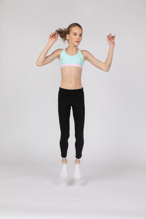 Vista frontal de una jovencita en ropa deportiva levantando las manos mientras salta